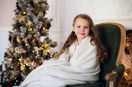 可爱的小女孩坐在圣诞树旁家里裹着温图片
