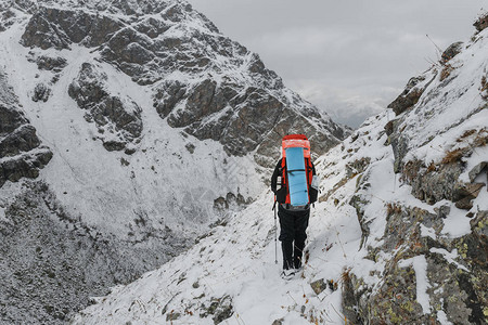 爬行者在山上悬崖和深渊背景的陡峭的雪覆盖斜坡上行走风险和户图片