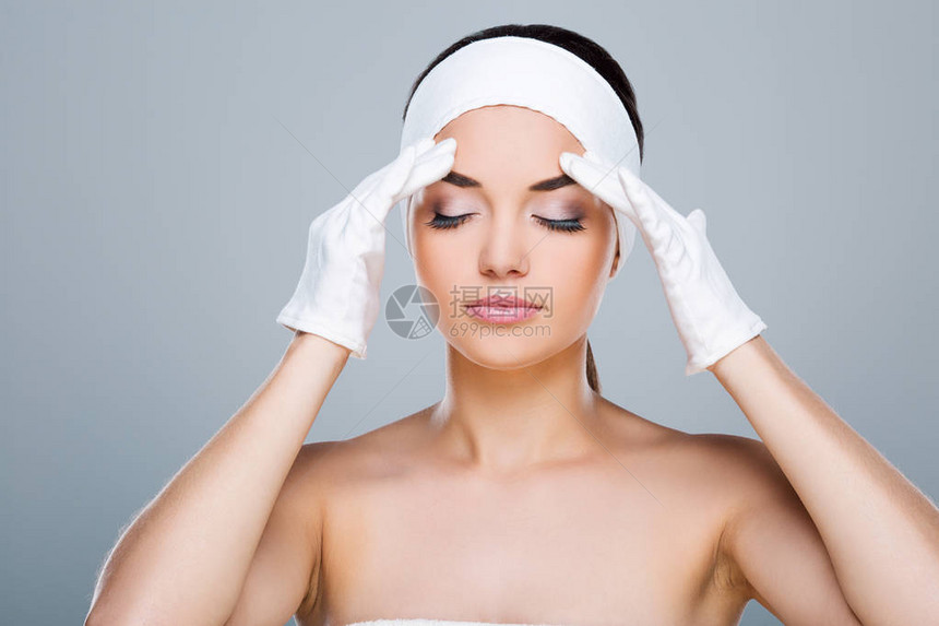 戴白色头巾的女人用白手套双手抚摸额头闭着眼睛的模特头和肩膀美容院图片