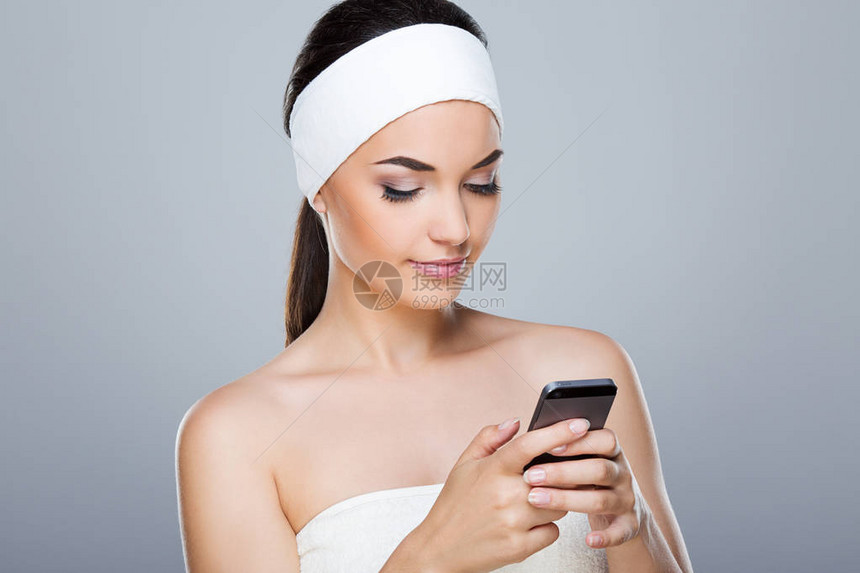 在白色头带拿着电话的模型看着电话和微笑的年轻女子头和肩膀美容院图片