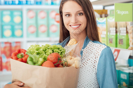 在超市购买纯素食品和新鲜蔬菜的年轻微笑女健康饮图片