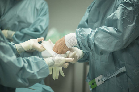 关节镜医院手术的外科医生在手术室急诊室的手术室中戴上无菌制服背景