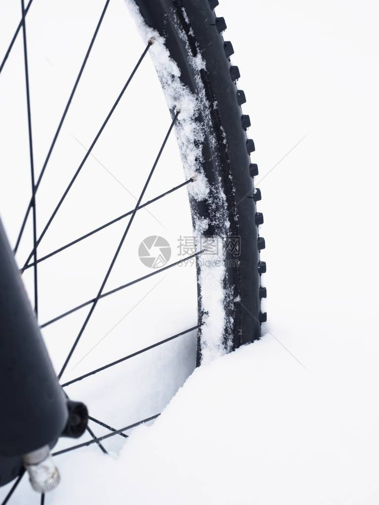 山地车前轮停留在粉雪中在深雪堆下迷失了道路雪花融化在黑暗的越野轮胎上在该领图片