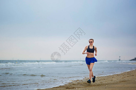 年轻的健身跑步女人在雾蒙的早晨在海洋或大海附近的海滩上快速慢跑健身和健康的背景图片