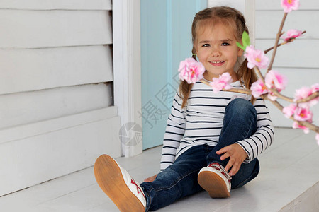 穿着牛仔裤和慢跑白鞋的漂亮小女孩坐在门的木白色门槛上图片