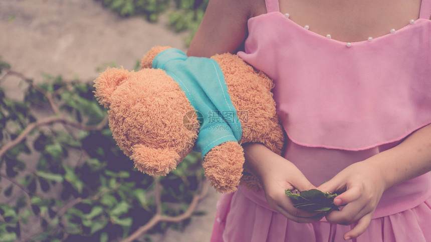亚洲女孩可爱的拥抱Teddy熊娃和绿叶图片
