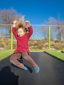 三岁快乐的金发孩子冬天穿红毛衣在野外游乐场跳图片
