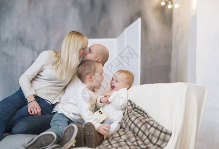 亲吻父母和坐在软沙发上坐在家里的小孩的肖像图片