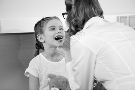 检查微笑的小女孩病人喉咙的女医图片