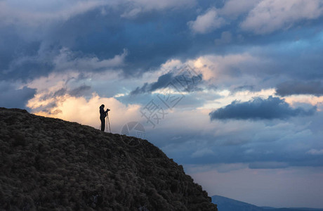山崖上的摄影师在寒冷的天气里用相机和三图片