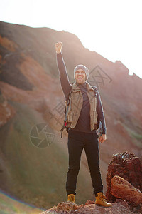 身穿时尚活跃的外装旅行者站在山顶上举起手抬起手图片