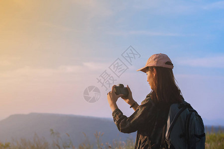 背着包在日出海边山峰拍照的亚洲女图片