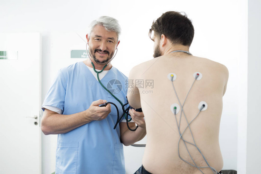医院背部贴有电刺激器电极的男患者微笑医生测图片