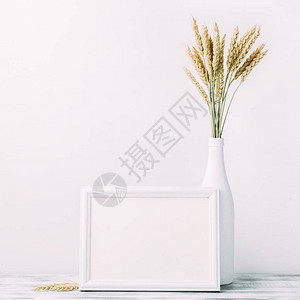 白色水平空框架与小麦花束在桌子上的白色花瓶带有复制空间背景图片
