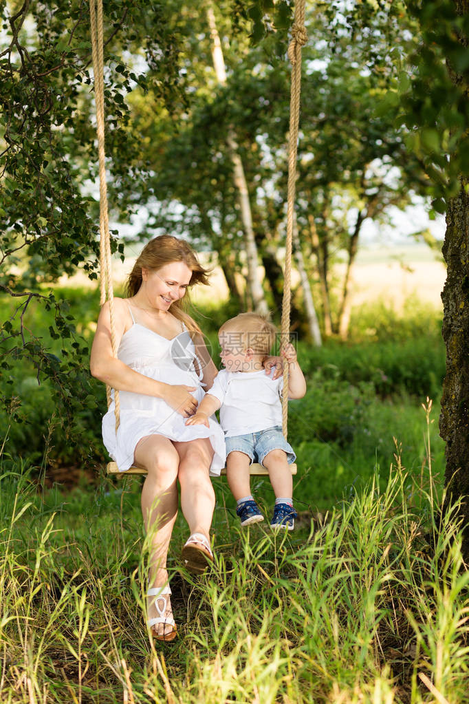 一个小男孩和他怀孕的母亲坐在秋千上怀孕的妈和一个男孩在草地上休息母亲和儿图片