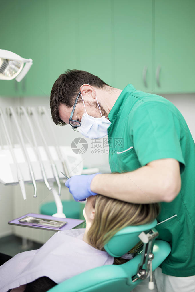 年轻妇女坐在牙医椅子上医生检查牙图片