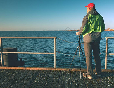 独自旅游者在木制码头板上用照相机和三脚架拍照图片