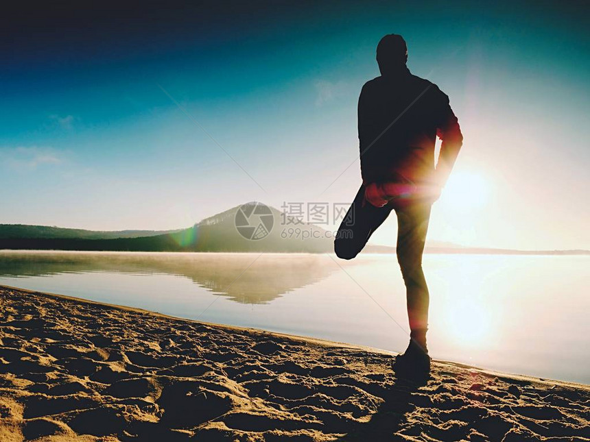 男人在沙滩上锻炼日出时在湖滩上锻炼和伸展的活跃男子的剪影健康的生活方式独自在早晨海滩锻炼的图片