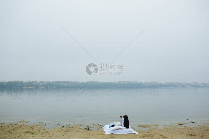 快乐的年轻家庭在湖边一起放松他们躺在白图片