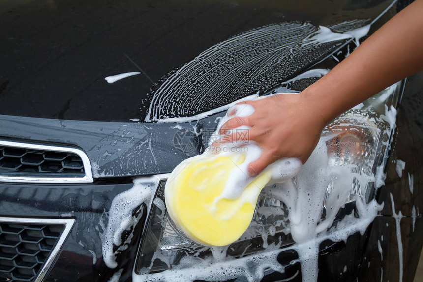 用黄色海绵和泡沫洗车的人手图片