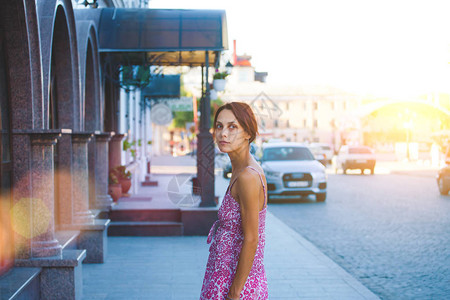 穿着粉红色裙子的年轻女人站在街上对着大楼和机器图片