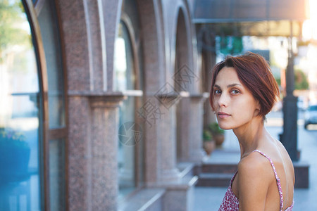 穿着粉红色裙子的年轻女人站在街上对着大楼和机器图片