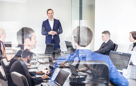 成功的团队领导和企业主在公司办公室领导商务会议在前景和玻璃反射的笔记本电脑上工作的商务人士商背景图片