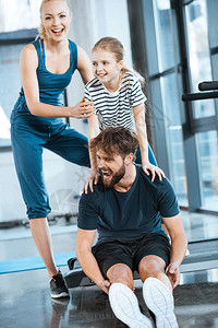 女孩抱着累了父亲坐在健身房的跑步机上的女人图片