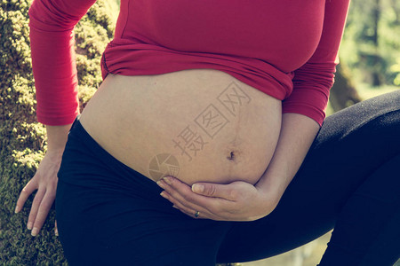 紧握着孕妇肚子的女手期待母亲成为图片