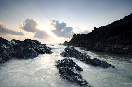 在美丽的日出背景上喷洒于独特岩石形成之上的巨浪图片