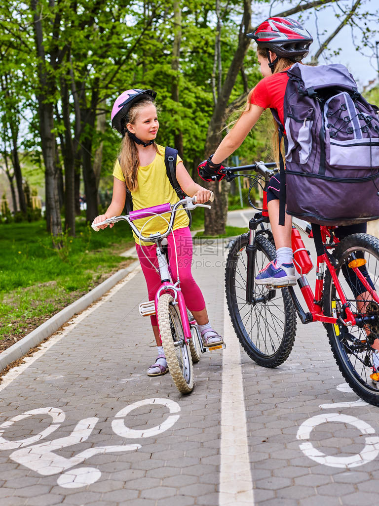 自行车道并与孩子们一起签名女孩们戴着背囊ciclyng骑自行车头盔孩子们在白色自行车道上替代城市交通迎图片