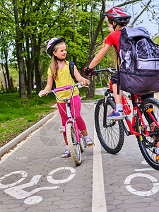 自行车道并与孩子们一起签名女孩们戴着背囊ciclyng骑自行车头盔孩子们在白色自行车道上替代城市交通迎背景图片