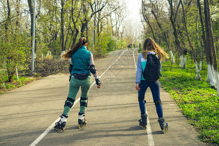 两个穿溜冰鞋的女孩骑着路走在彼图片
