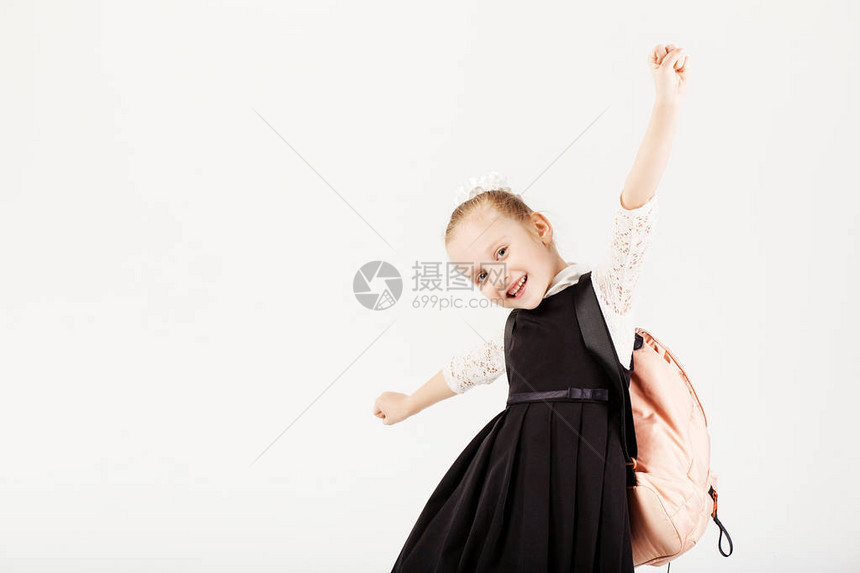 有趣的微笑小女孩背着大背包跳跃和在白色背景下玩乐看着相机学校理图片