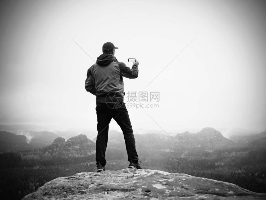 男人在岩石帝国的顶峰上用智能手机拍照图片
