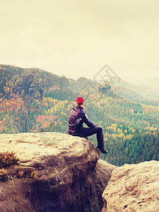 穿着黑色户外衣服的男人坐在破裂的岩石帝国上秋天创辉景观砂岩山惆怅雾图片