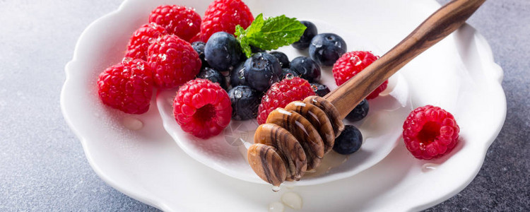 新鲜的蓝莓和草莓与蜂蜜放在白盘上图片