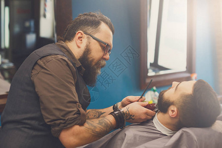 理发师在理发店用修剪器理发剪胡须男图片