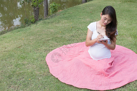 怀孕的亚洲孕妇写下笔记本上的笔记图片
