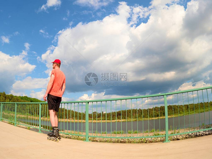 身穿红色t恤和黑色裤子的直排轮滑运动员在桥上滑冰的后视图在湖桥上光滑的混凝土地面上进行户外直排轮滑穿四轮靴图片