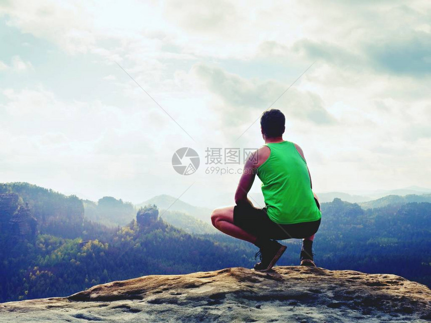 穿着绿色背心和黑色短裤的游客蹲在岩石上图片
