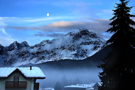 以雪山月亮和山间小屋为特色的黄昏冬季景观图片