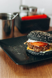 黑盘子里有西红柿和奶酪的黑鱿鱼墨汁汉堡图片