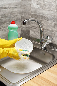 用黄色防护橡胶手套清洗餐具的女手的特写图片