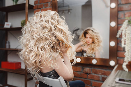 美容院里的金发女人用灯看着镜子里的倒影图片