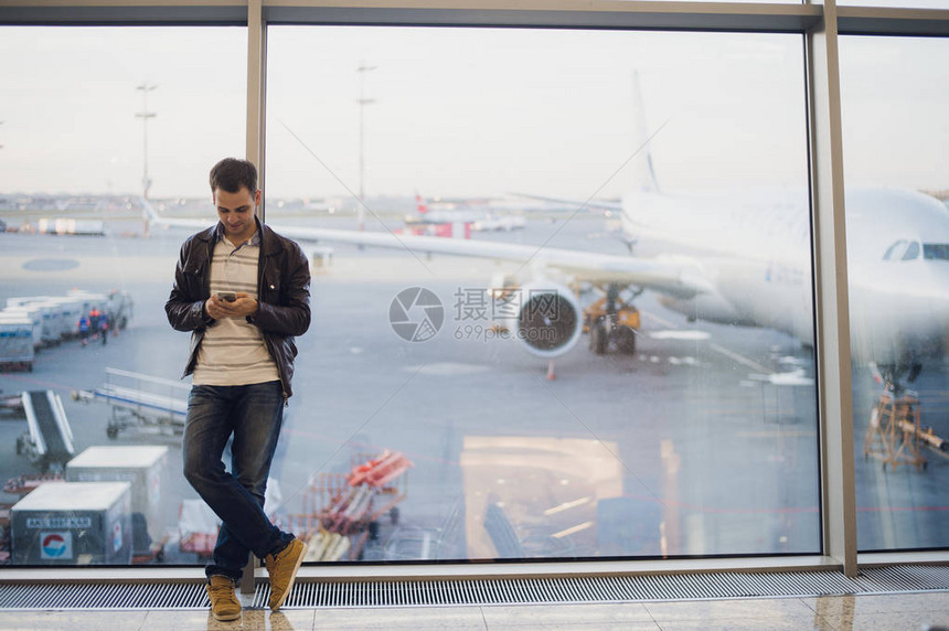青年男子使用手机等待航班的飞行时间图片