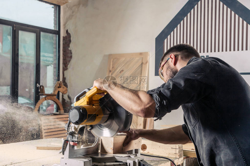 一位年轻的男建筑木匠在车间里用木板锯现代圆锯图片