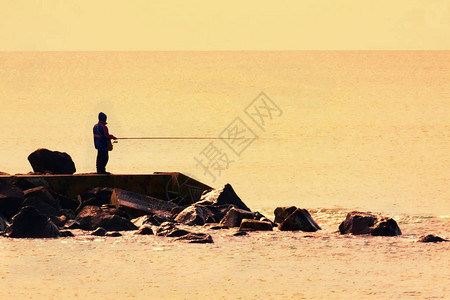 日落时悬崖上的渔夫图片