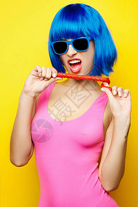 在假发太阳镜和粉红色泳衣有乐趣在黄色上吃棒棒糖的感美女图片