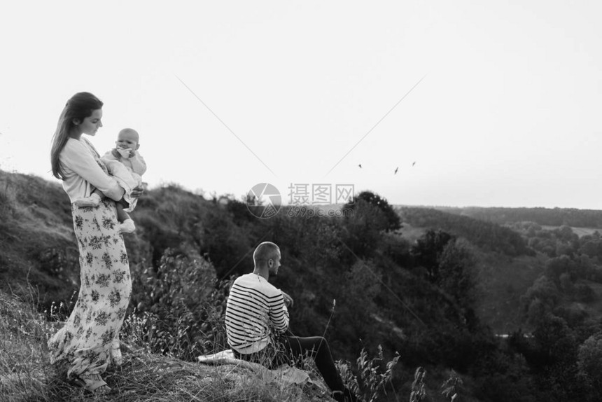 年轻的家庭带着小女儿在高草上的山坡上行走母亲把女儿抱在夕阳的手图片